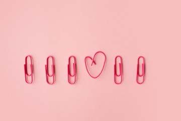 Several pink paper clips in a row. One heart shaped.