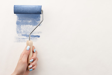 Female hand painting wall with roller in blue color, copy space