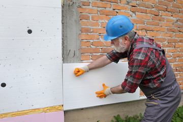 Worker placing styrofoam insulation to brick wall, house renovation