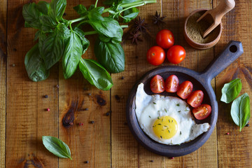 Fried eggs in a pan. Basil, spices, tomatoes and a frying pan with an egg on the table.