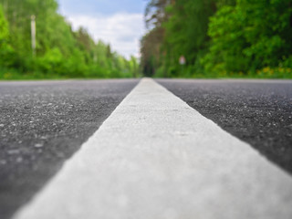 Two-way asphalt road in the countryside, woodland, close-up of the dividing strip. Highway perspective goes into the green forest.