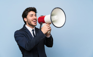 Businessman over isolated blue wall shouting through a megaphone