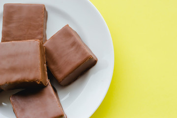 Chocolate sweets on a plate on a yellow background.