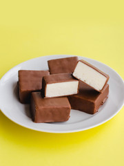 Chocolate sweets with white souffle on a plate on a yellow background.
