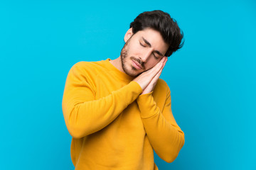 Handsome over isolated blue wall making sleep gesture in dorable expression