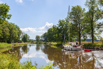 Sailboat on an idyllic canal lined with lush trees in summer