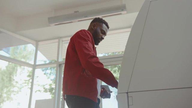 African american attractive man getting money from an ATM cash machine with a credit card inside the bank.