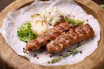 Traditional Adana kebab on wooden plate with marinated onion garnishing and spicy aromatic herbs. Delicious meat, Turkish cuisine
