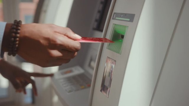 Afro-american businessman taking money from ATM cash machine removing a credit card. Close-up view of man using cashpoint machine inside the bank.