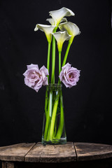 bouquet of yellow tulips and violet rose in vase on black background