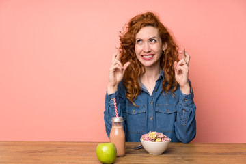 Redhead woman having breakfast cereals and fruit with fingers crossing