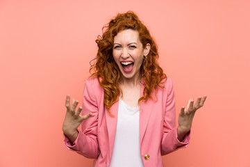 Redhead woman in suit over isolated pink wall unhappy and frustrated with something