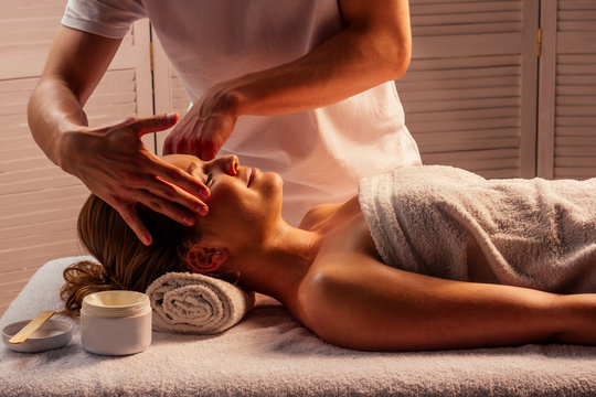 Young Woman Enjoys Ayurvedic Facial Massage In Luxury Resort Dark Lighting