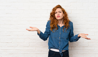 Redhead woman over white brick wall unhappy for not understand something