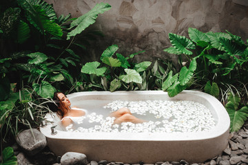 Woman relaxing in round outdoor bath with tropical flowers, organic skin care, luxury spa hotel,...