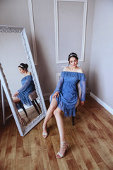 A beautiful woman in a blue dress is sitting on a velvet armchair studio shot