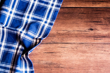 Checkered blue napkin on an old wooden brown background, top view. Image with copy space. Kitchen table with a towel - top view with copy space.