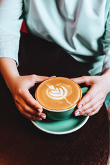 Female hands holding cyan cup of coffee cappuccino.