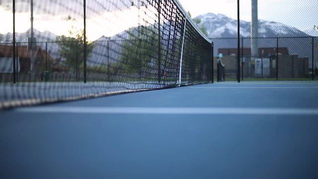 Shot of a tennis net on an empty tennis court. The net is slightly moving because of a slight breeze.