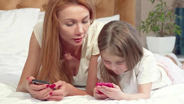 Mother teaching her daughter using smart phone. Adorable little girl learning using mobile phone with her mom. Beautiful woman enjoying weekend at home with her child 