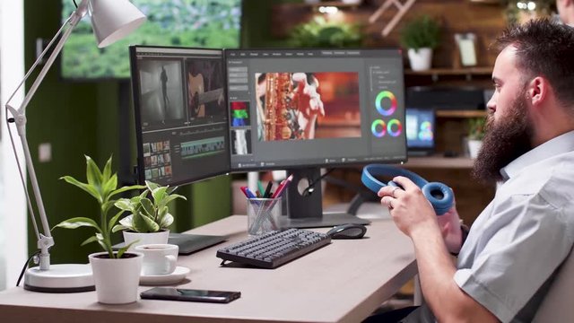 Medium shot of video editor working on new project in professional software. He puts his headphones on