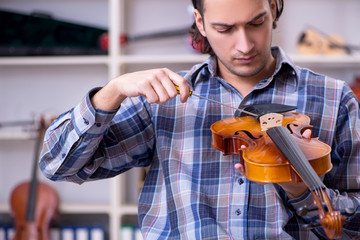 Young handsome repairman repairing violin