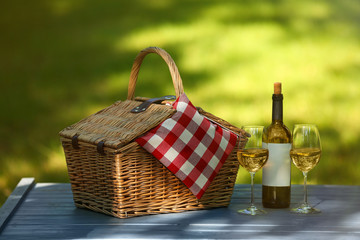 Wicker basket with blanket and wine on table in park. Summer picnic