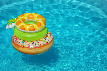 Stack of colorful inflatable rings floating in swimming pool on sunny day. Space for text
