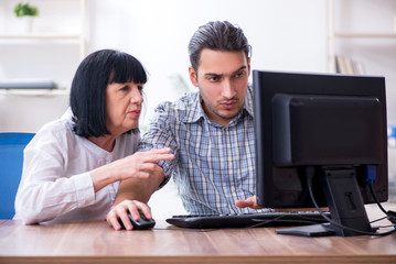 Young male employee explaining to old female colleague how to us