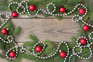 Christmas card concept with fir tree branches, red baubles and silver bead chain on wooden background, deep side shadows - text space