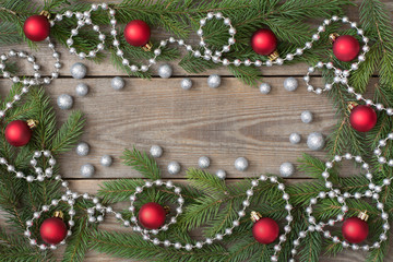 Christmas card concept with fir tree branches, red baubles, brocade globules and silver bead chain wooden background, deep side shadows - text space