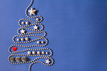 Christmas tree concept with silver bead chain, silver stars, cones,  globules and red heart on dark blue background, deep shadows - text space