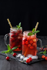 Fresh summer cocktail with sweet cherry and ice cubes on a dark background on a black wooden table.