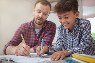 Cropped shot of a happy charming schoolboy smiling joyfully, drawing with his teacher during art class. Teacher helping his little student with artistic assignment