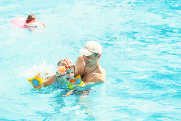 Little girl learning how to swim with swimming instructor. Happy smiling father and daughter...