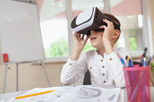 Fototapeta Technology, modern childhood concept. Little boy looking overwhelmed and excited, wearing 3d virtual reality glasses for the first time at school, copy space. Young schoolboy wearing vr headset, looki