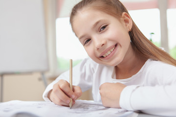 Close up of a beautiful happy schoolgirl smiling to the camera while drawing at school, copy space