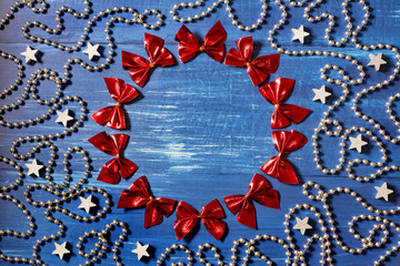 Christmas decoration with a cirle of red ribbons, silver bead chain and stars on dark blue wooden background - place for text, deep shadows