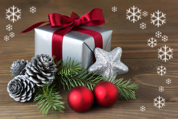 Christmas composition: a gift wrapped with red ribbon, silver cones, red baubles and a fir tree branch - isolated on wooden background