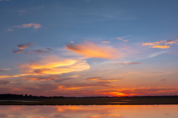 Fototapeta premium Sunset reflection lagoon. beautiful sunset behind the clouds and blue sky above the over lagoon landscape background. dramatic sky with cloud at sunset