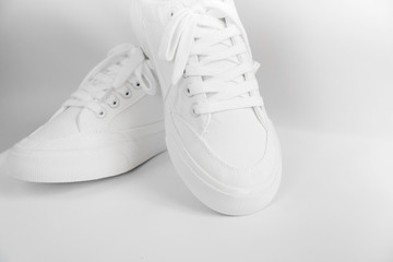 New white female or teen sneakers isolated on white background. White textile sneakers with rubber soles with tied laces on a light gray background. Use for banners, promotional flyers