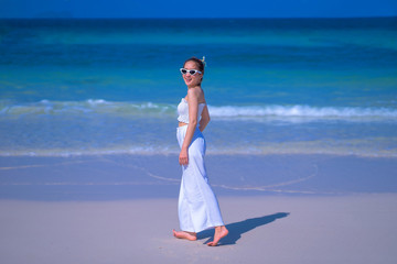 Fototapeta na wymiar Summer photo of stylish pretty woman in sunglasses, wearing white dress, enjoying the summer days, on the sand beach, near the sea