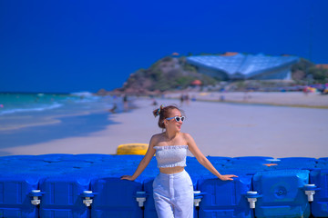 Summer photo of stylish pretty woman in sunglasses, wearing white dress, enjoying the summer days, on the sand beach, near the sea