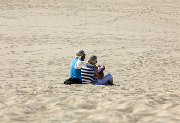Fototapeta premium A couple of people are resting on the Dune of Pilat, the tallest sand dune in Europe. La Teste-de-Buch, Arcachon Bay, Aquitaine, France