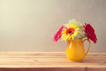 Colorful flower bouquet in yellow jug on wooden table.