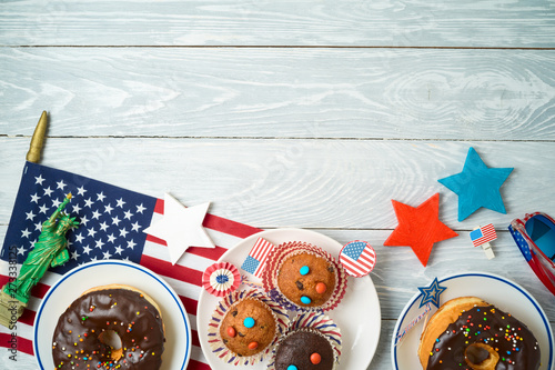 Happy Independence Day, 4th of July celebration concept with cupcakes, donuts and american flag on wooden background.