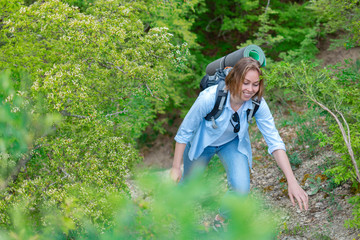 Smiling woman climbing on a mountain path. Plants and trees in the background. Active sports and tourism. Tint