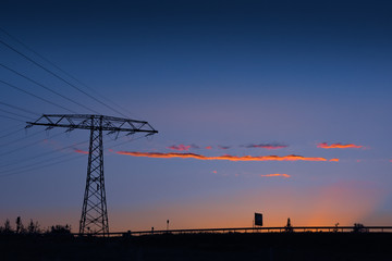 Electricity pylon and power lines at sunset silhouetted against a colorful orange and blue twilight sky with copy space