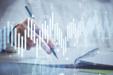 Financial forex graph displayed on hands taking notes background. Concept of research. Double exposure