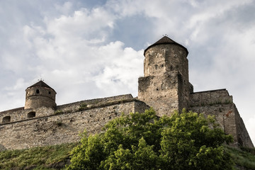 Fototapeta na wymiar Two towers and stone walls of the medieval Kamianets-Podilskyi fortress of the XVI century on a hill on the background of a blue sky. Ukraine.